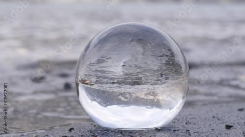 View of Swiss mountains in a lens ball lying in the sand on a beach.