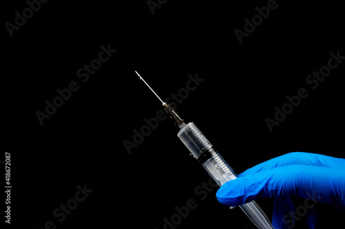 Two fingers and a full syringe on a black background