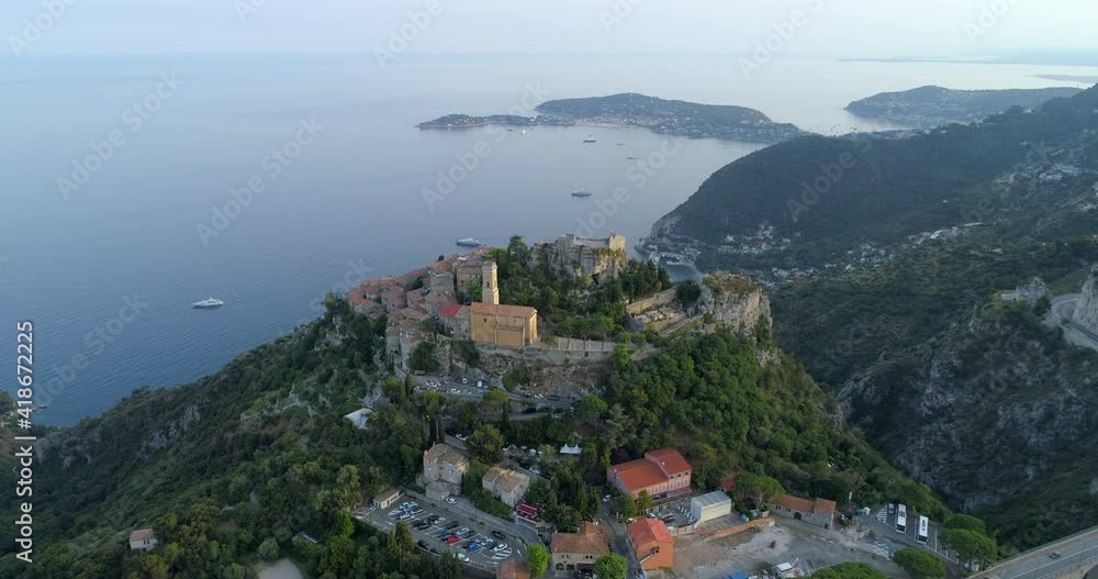 Aerial shot of Catholic church in city by sea, drone ascending backward from buildings on mountain against sky during sunset - C�te d'Azur, France Aerial shot of Catholic church in city by sea, drone ascending backward from buildings on mountain against sky during sunset - C�te d'Azur, France