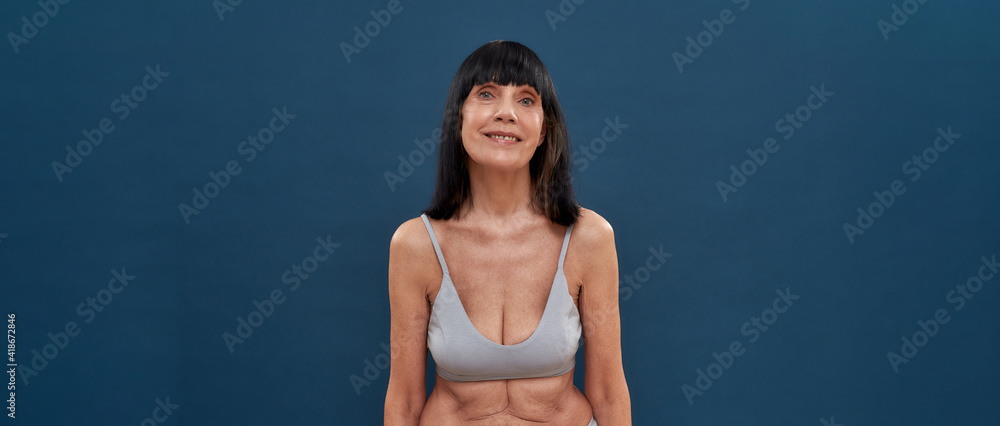Feeling young at any age. Beautiful middle aged caucasian woman with age wrinkles around eyes posing on dark blue background, panoramic banner with copy space for text Feeling young at any age. Beautiful middle aged caucasian woman with age wrinkles around eyes posing on dark blue background, panoramic banner with copy space for text