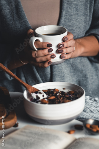 A young woman drinks morning coffee, eats a healthy breakfast and reads a book. Morning routine. Stylish manicure. Correct habits. Holding a cup in his hands