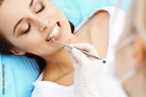 Young female patient visiting dentist office.Beautiful woman with healthy straight white teeth sitting at dental chair with open mouth during oral checkup while doctor working at teeth