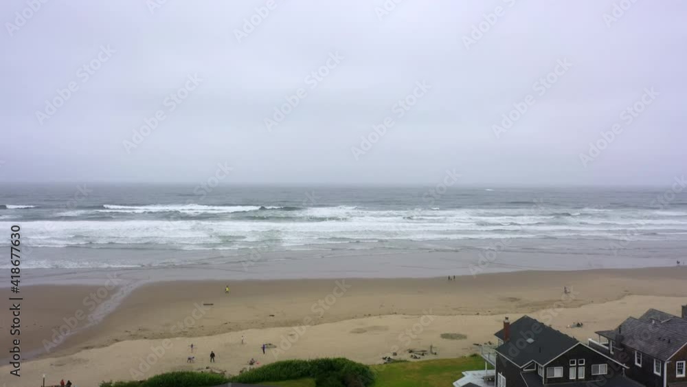 Aerial shot of houses and people at beach against cloudy sky, drone ascending near coastline - Cannon Beach, Oregon Aerial shot of houses and people at beach against cloudy sky, drone ascending near coastline - Cannon Beach, Oregon