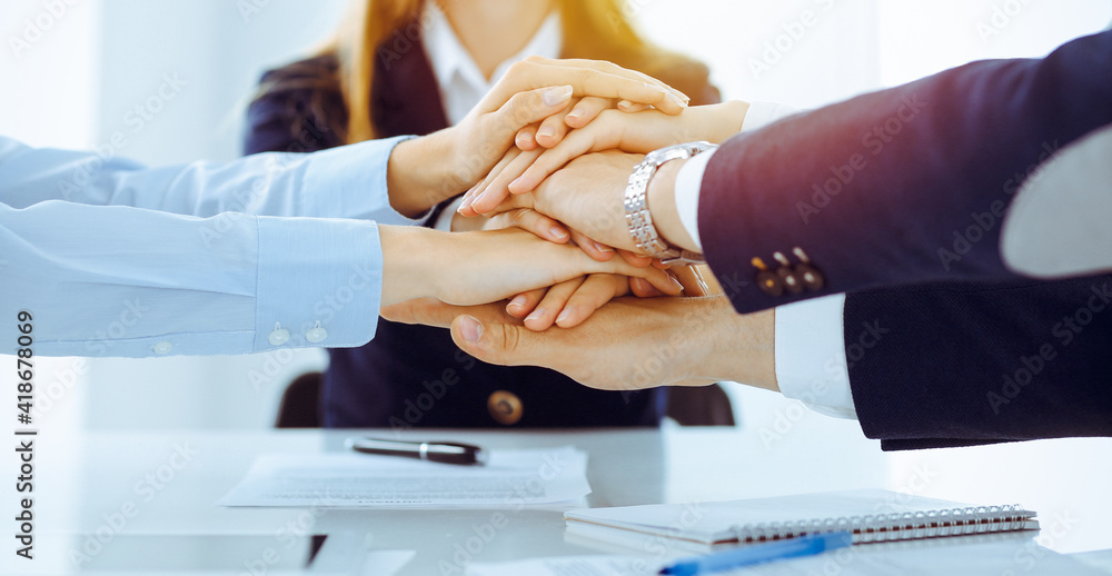 Obraz premium Business team showing unity with their hands together in sunny office. Group of people joining hands and representing concept of friendship and teamwork