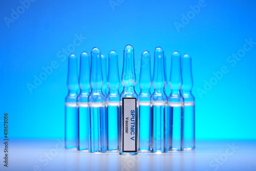 Glass ampoule with the inscription Sputnic V on the background of other ampoules lined up on a blue background. Society Immunization and Vaccination Concept photo