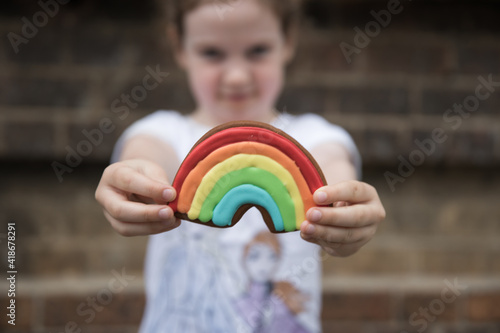 A young child holding a colorful rainbow cookie
