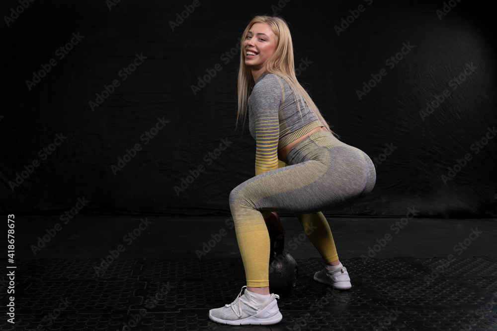 Fototapeta premium athletic girl with blond hair squats holding a large kettlebell