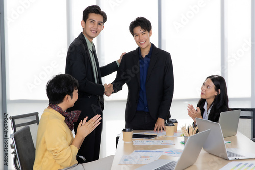 Tomboy good looking executive woman happy with success and shaking hands with Asian businessman in office white the team cheer up, laugh and congratulation with them