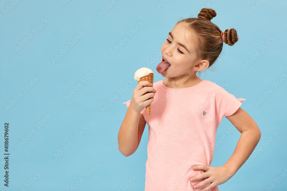 happy little girl eating vanilla ice cream in a waffle cone on blue background. copy space for text happy little girl eating vanilla ice cream in a waffle cone on blue background. copy space for text