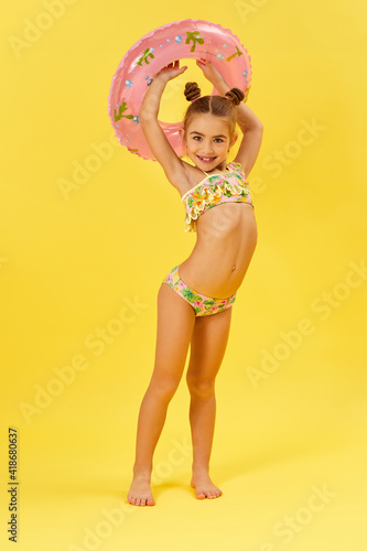 Wallpaper Mural cute little child girl in swimwear with inflatable rubber circle on yellow backg