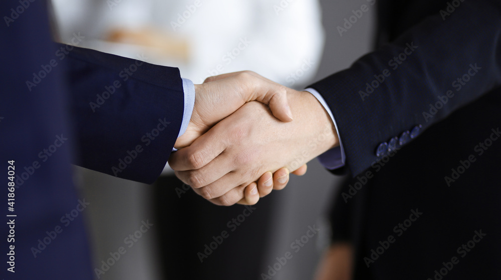 Business people shaking hands at meeting or negotiation, close-up. Group of unknown businessmen and a woman stand together in a modern office. Teamwork, partnership and handshake concept