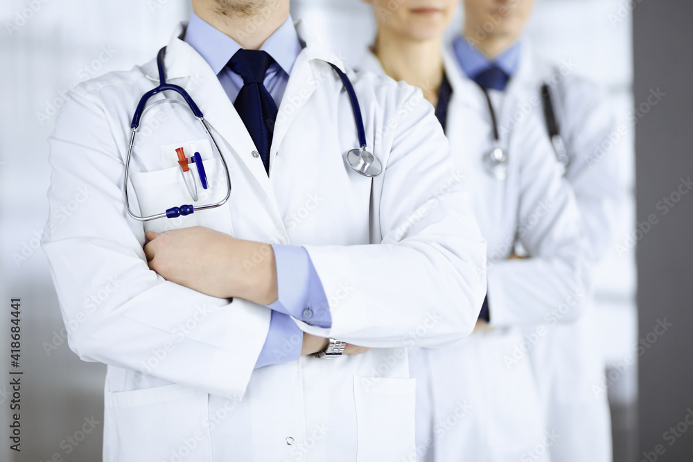 Group of modern doctors standing as a team with crossed arms and stethoscopes in hospital office. Physicians ready to examine and help patients. Medical help, insurance in health care, best desease Group of modern doctors standing as a team with crossed arms and stethoscopes in hospital office. Physicians ready to examine and help patients. Medical help, insurance in health care, best desease