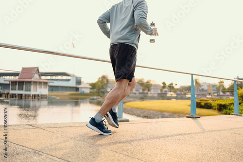 Young sport man hold water bottle while jogging and running on the road in the park.