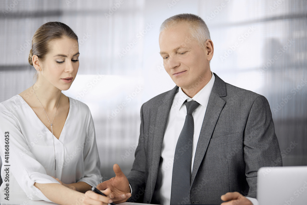 Elderly businessman and woman sitting and communicating in office. Adult business people or lawyers working together as a partners and colleagues at meeting. Teamwork and cooperation concept Elderly businessman and woman sitting and communicating in office. Adult business people or lawyers working together as a partners and colleagues at meeting. Teamwork and cooperation concept