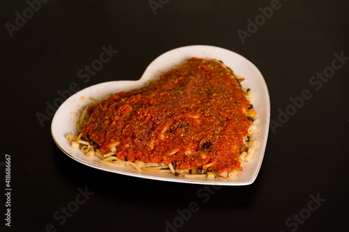 Famous traditional Arabic, Egyptian dish - Koshari. National Kushari in a white heart plate on dark wooden background with tomato sauce