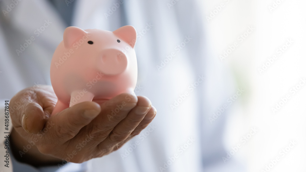 Crop close up of male doctor hand hold piggybank for charity contribution or fee into clinic budget. Mature man GP or medical specialist ask for volunteer donation for patients needs. Welfare concept. Crop close up of male doctor hand hold piggybank for charity contribution or fee into clinic budget. Mature man GP or medical specialist ask for volunteer donation for patients needs. Welfare concept.