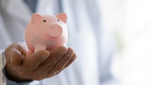 Crop close up of male doctor hand hold piggybank for charity contribution or fee into clinic budget. Mature man GP or medical specialist ask for volunteer donation for patients needs. Welfare concept.