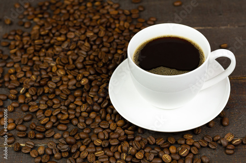 Black coffee in white ceramic cup and coffee bean on wooden background.