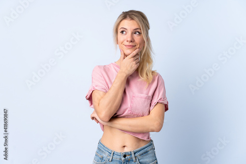 Blonde woman over isolated blue background thinking an idea while looking up
