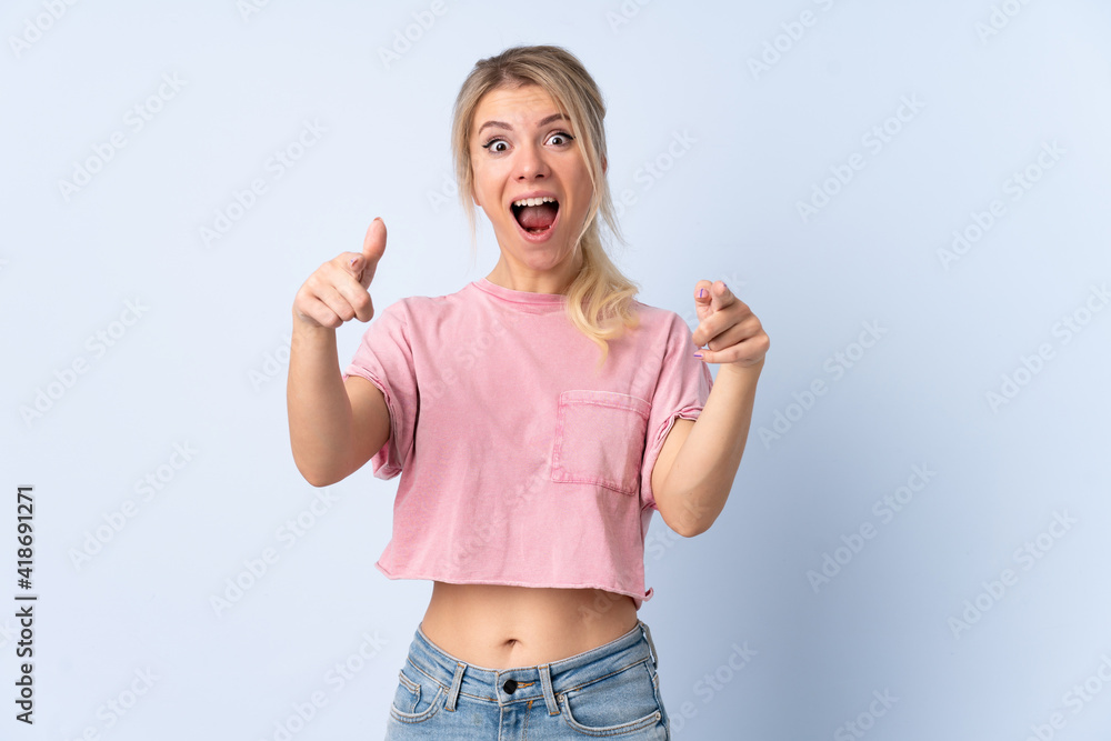 Blonde woman over isolated blue background surprised and pointing front Blonde woman over isolated blue background surprised and pointing front