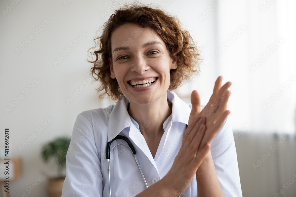Headshot portrait of smiling young Caucasian female doctor look at camera talk on video call with patient. Happy woman GP have online webcam consultation with hospital client on computer.