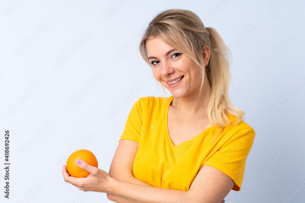 Blonde woman over isolated blue background holding an orange Blonde woman over isolated blue background holding an orange