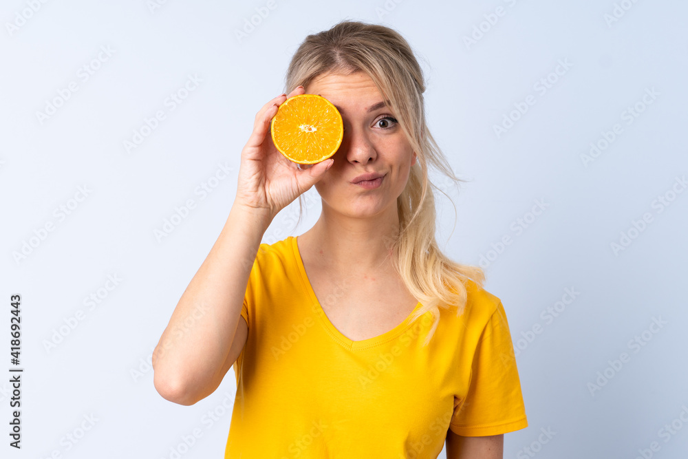 Blonde woman over isolated blue background holding an orange Blonde woman over isolated blue background holding an orange