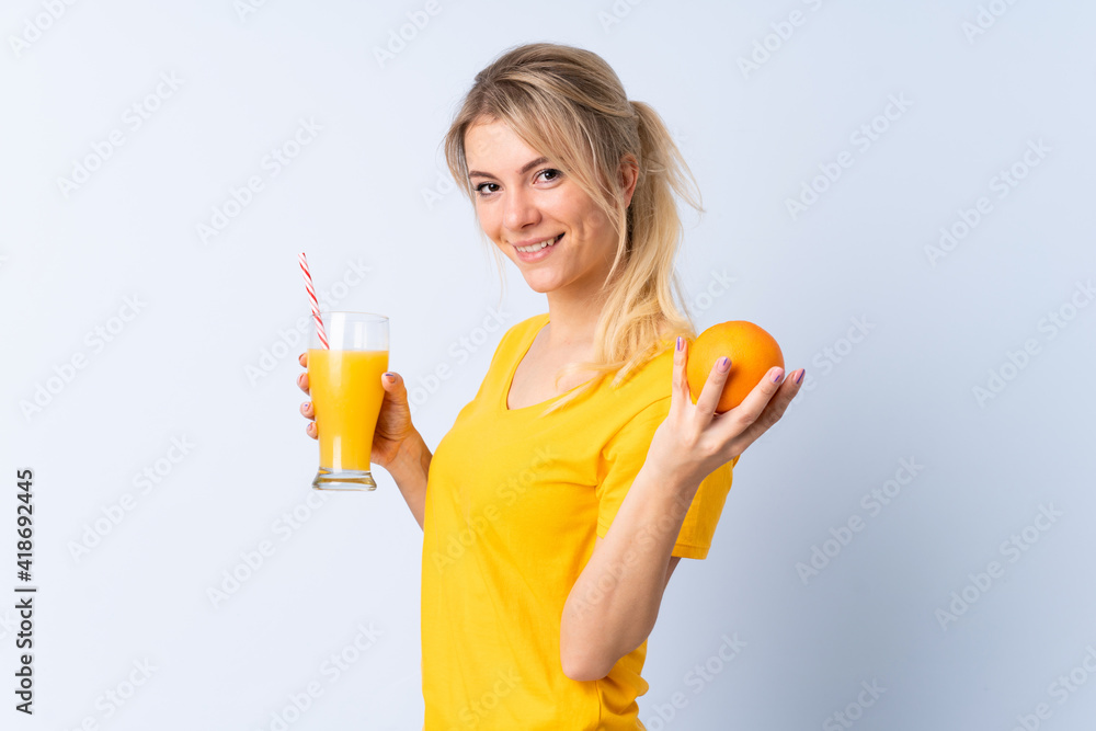 Blonde woman over isolated blue background holding an orange and an orange juice Blonde woman over isolated blue background holding an orange and an orange juice