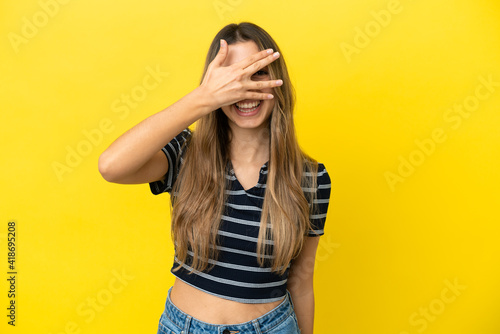Young caucasian woman isolated on yellow background covering eyes by hands and smiling