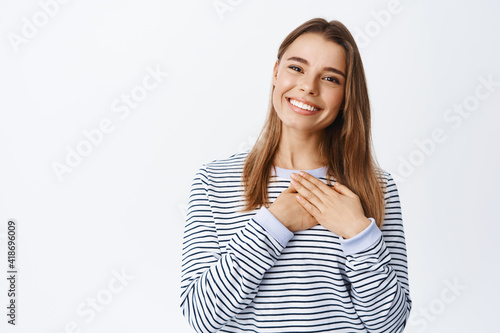 Картината върху платно Portrait of blond smiling woman holding hands on heart, looking with thankful fa