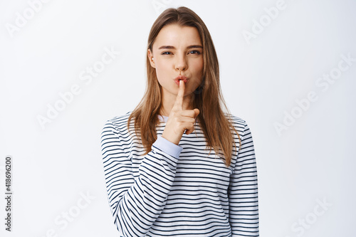 Slika na platnu Image of young blond girl shushing at camera, telling a secret, asking to keep s