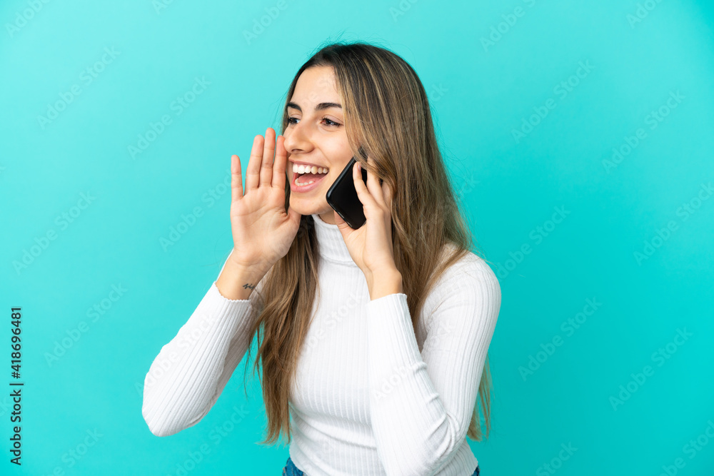 Young caucasian woman using mobile phone isolated on blue background shouting with mouth wide open to the side Young caucasian woman using mobile phone isolated on blue background shouting with mouth wide open to the side