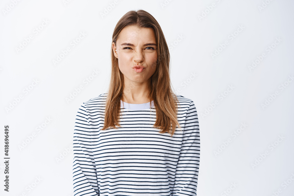 Sassy beautiful girl with blond hair, making funny face and screw nose silly, express happy and positive emotions, standing over white background
