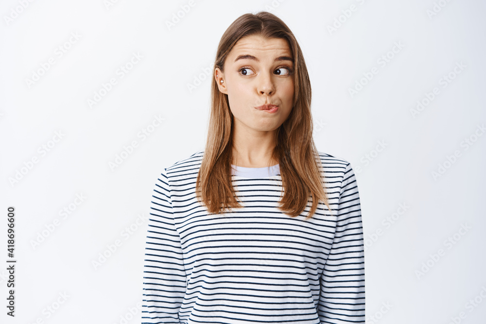 Portrait of intrigued blond girl checking out something interesting, pucker lips and looking left with tempted face, wants to try something, white background Portrait of intrigued blond girl checking out something interesting, pucker lips and looking left with tempted face, wants to try something, white background