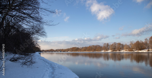 Winter landscape with a river. River and bank covered with snow. River along the horizon, trees and branches near the shore.