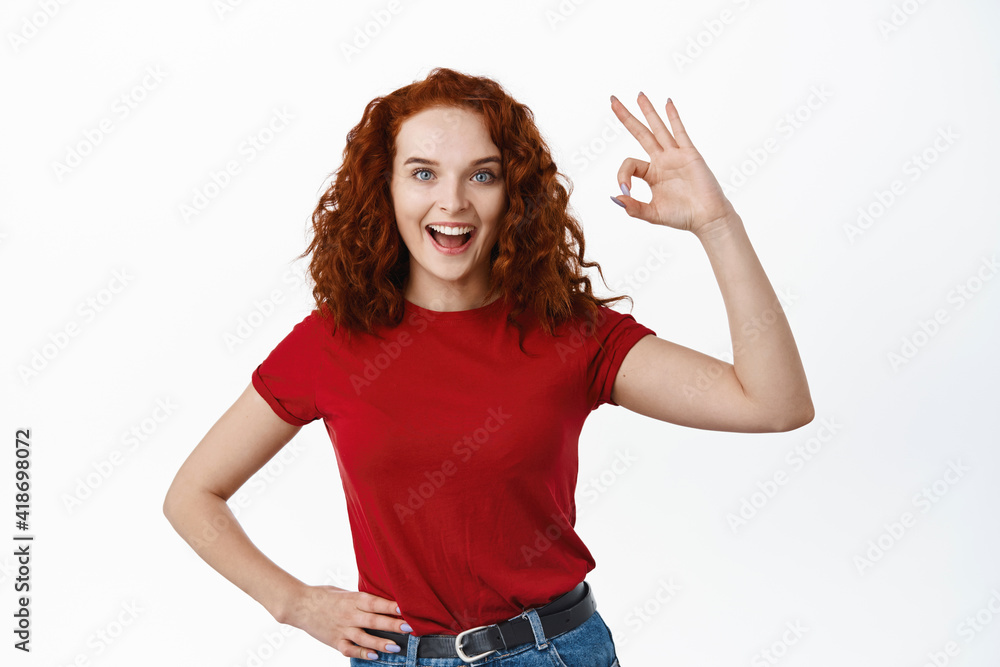 Excellent job. Pleased redhead girl with curly hair say alright yes, showing Okay sign and smiling satisfied, approve good thing, standing over white background Excellent job. Pleased redhead girl with curly hair say alright yes, showing Okay sign and smiling satisfied, approve good thing, standing over white background