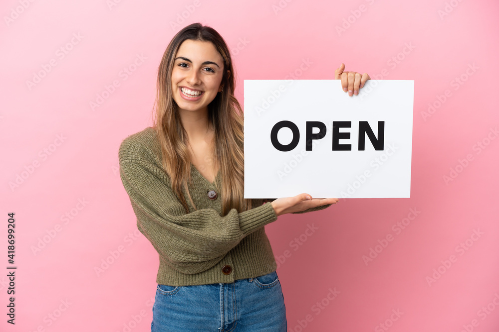 Young caucasian woman isolated on pink background holding a placard with text OPEN with happy expression Young caucasian woman isolated on pink background holding a placard with text OPEN with happy expression