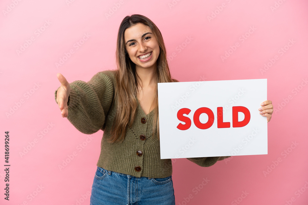 Young caucasian woman isolated on pink background holding a placard with text SOLD making a deal Young caucasian woman isolated on pink background holding a placard with text SOLD making a deal
