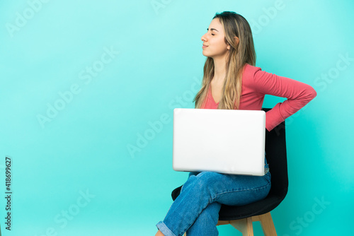 Young caucasian woman sitting on a chair with her pc isolated on blue background suffering from backache for having made an effort © luismolinero