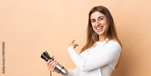 Woman using hand blender over isolated background pointing back