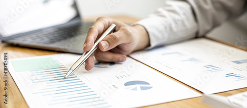 A close-up view of a businessman holding a pen pointing at a bar chart on a company financial document prepared by the Finance Department for a meeting with business partners. Financial concept. photo