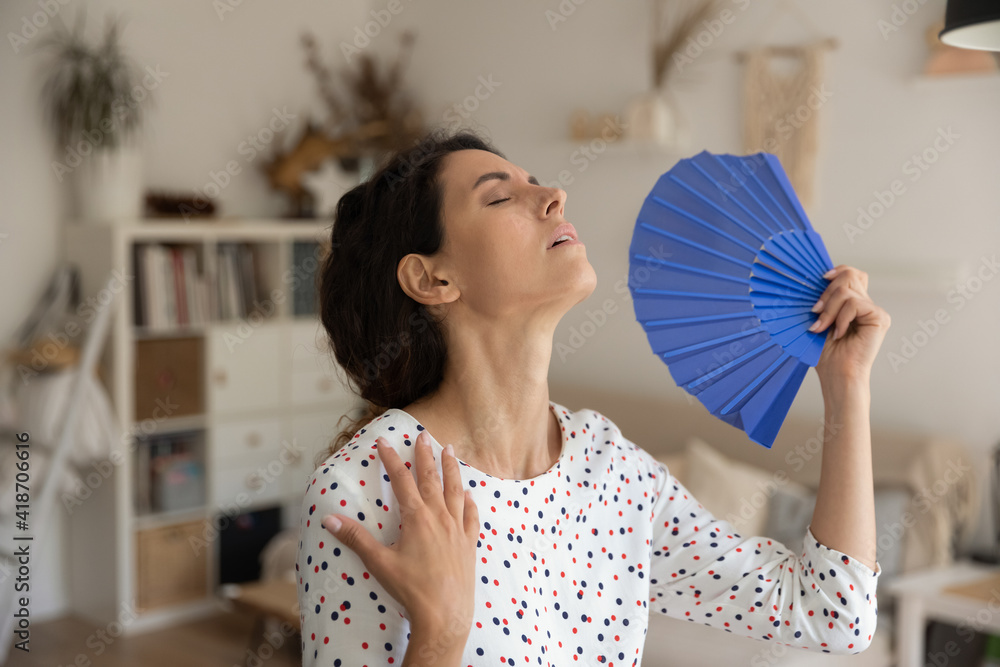 What a heat. Exhausted young female housewife suffer from extra hot temperature at home apartment wave herself use hand weaver. Overheated millennial woman cool air with paper fan miss air conditioner - obrazy, fototapety, plakaty 