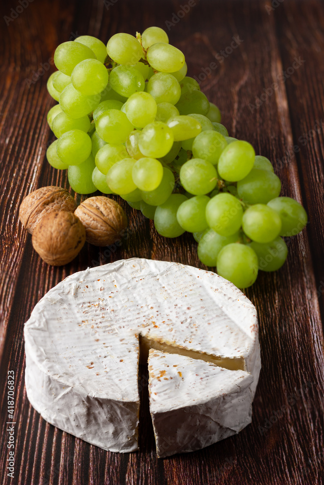 Camembert with green grapes and walnut on wooden table.