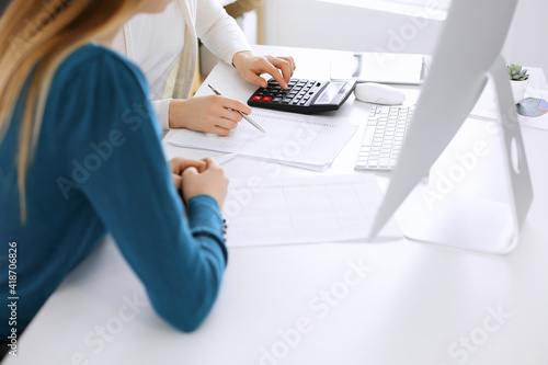 Accountant checking financial statement or counting by calculator income for tax form, hands close-up. Business woman sitting and working with colleague at the desk in office. Audit concept © Iryna