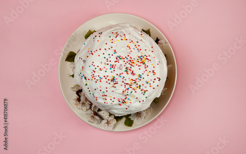 Easter composition. A glazed Easter cake decorated with sugar sprinkles and apricot flowers on a white plate stands on a pastel pink background. Happy Easter Holidays. Top view.