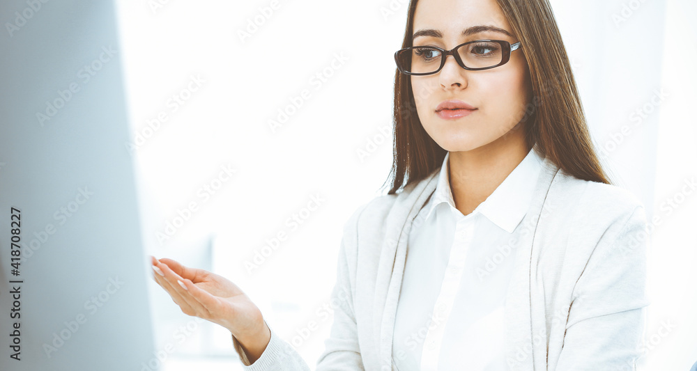 Young woman sitting at the desk with computer in white colored office. Looks like student girl or business lady communicating with casual dressed man Young woman sitting at the desk with computer in white colored office. Looks like student girl or business lady communicating with casual dressed man
