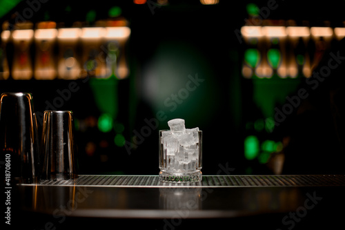 Gorgeous view of glass with ice standing on bar counter on blurred background