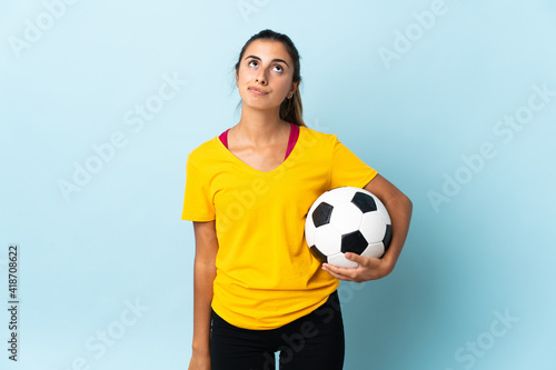 Young hispanic football player woman over isolated on blue background and looking up © luismolinero