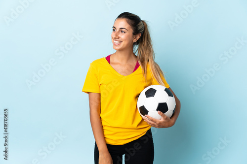 Young hispanic football player woman over isolated on blue background looking to the side and smiling © luismolinero