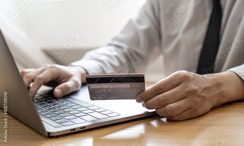 A guy holds a credit card and is filling out his credit card information on his laptop to place an order on the website. Credit cards can be used to pay for goods or services with online merchants.